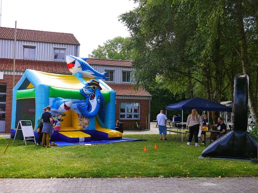 Hüpfburg mit Wassermotiven und Zelt, umgeben von Menschen im Freien.