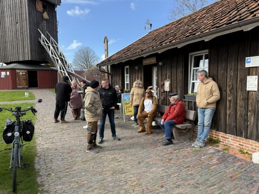 Entspannung vor dem Müllerhaus Gruppe von Menschen vor traditionellen Holzgebäuden und einer Windmühle.