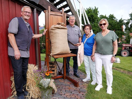 Vier Personen stehen mit einem Sack an einer Holzkonstruktion vor einem roten Gebäude.