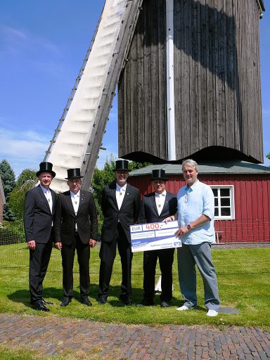 Fünf Männer in Anzügen und Zylindern stehen vor einer Windmühle.