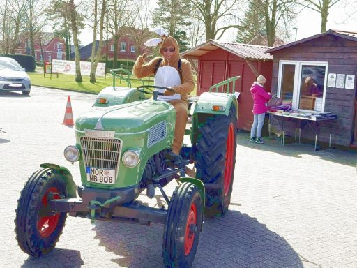Osterhase Wilhelm reist zünftig mit einem Trekker an Eine Person in Arbeitskleidung sitzt auf einem alten grünen Traktor und winkt.