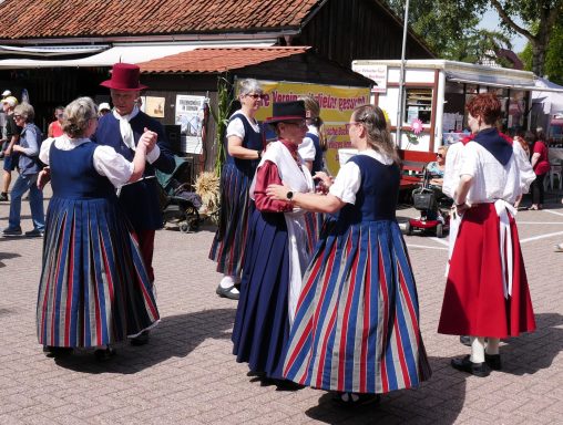 Frauen in traditioneller Tracht tanzen auf einem Fest im Freien.